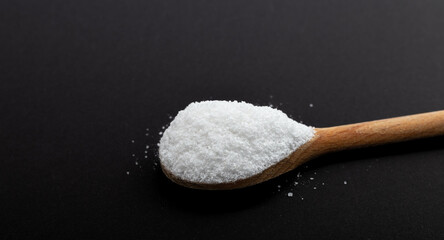 Iodated salt scoop in front of black background with wooden spoon. Textured horizontal photo, closeup. V37.