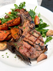 Grilled pork chop with roasted sweet potatoes, garlic, cherry tomatoes and fresh arugula. Gourmet meat dish concept.