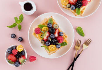 Sweet Belgian waffles with fresh berries and maple syrup on pink background. Top view. Desserts. 