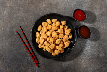 Golden crispy chicken popcorn with ketchup and sweet chili on a gray background. Top view. Fast food and snack concept.