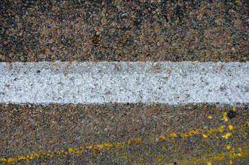 Gritty asphalt road with bold white and yellow lines creating a textured surface for backgrounds or abstract urban designs and transportation concepts