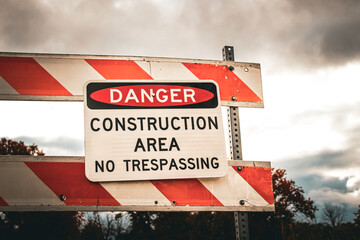 Obraz premium Closeup of a DANGER CONSTRUCTION AREA NO TRESPASSING sign mounted on a striped barrier. Infrastructure and development background or design element.