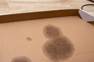 A close-up view of a brown cardboard box showing dark stains on its surface, possibly from food or...
