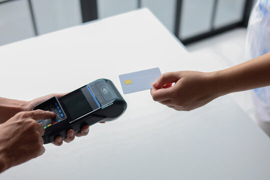 A customer is holding a white credit card with a chip tapping near a point-of-sale (POS) terminal for make contactless payment. People and modern technology concepts. - Powered by Adobe