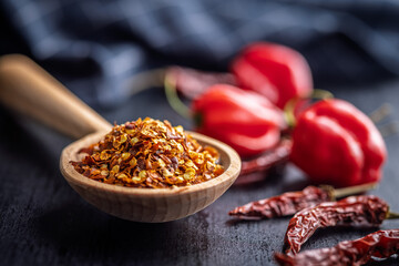 Red chili peppers flakes. Milled spicy peppers on wooden scoop on black table.