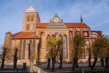 St. Nicholas Church in sunshine, with red roofs, tall windows, and autumnal trees in the foreground