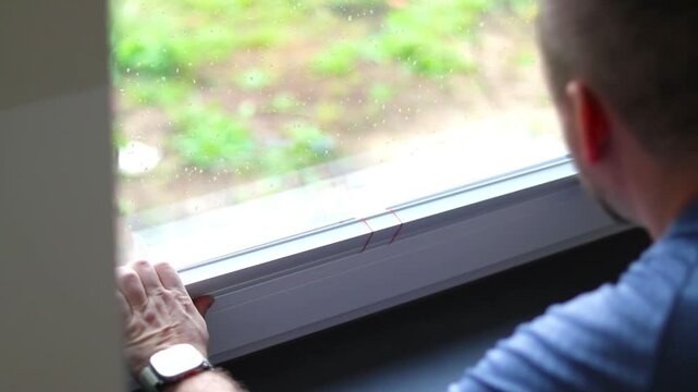 Close up of a caucasian man installing white blinds on kitchen window in a house, modern plisses shades from sunlight 