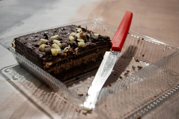 Half eaten chocolate cake and a knife with a red handle in a plastic box