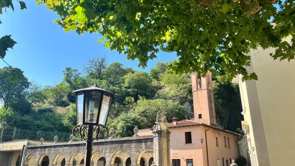 Italian Historical Building Amidst Lush Foliage: A charming antique lantern illuminates a classical architectural building framed by vibrant green leaves.