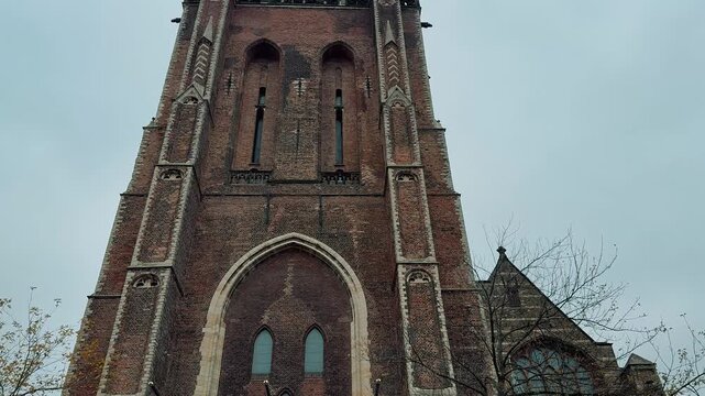 The immense tower of Delft's New Church dominates the market square under a cloudy sky. This Gothic structure is a major Dutch landmark.