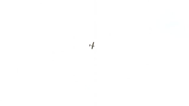 Minimalist shot of a small agricultural propeller plane flying in a bright white overcast sky. High-key aviation background with a tiny biplane soaring in empty space.
