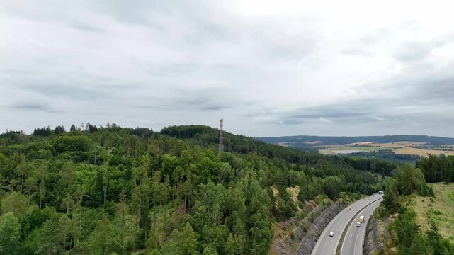 Aerial drone view of telecommunications tower rising above dense forest landscape. Cellular infrastructure antenna providing wireless communication network coverage in remote natural environment.