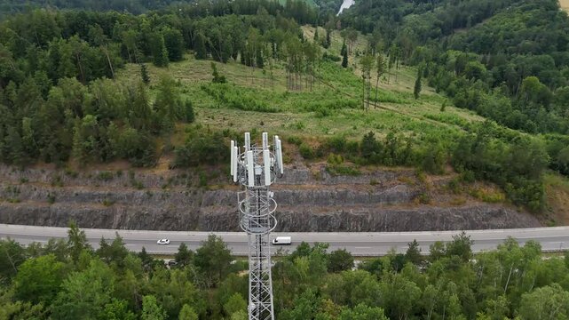 Aerial drone view of telecommunications tower rising above dense forest landscape. Cellular infrastructure antenna providing wireless communication network coverage in remote natural environment.