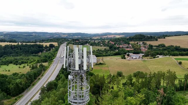Aerial drone view of telecommunications tower rising above dense forest landscape. Cellular infrastructure antenna providing wireless communication network coverage in remote natural environment.