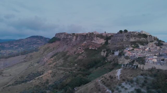 Aerial view: ancient village of Gerace Calabria Italy built on rocky mountain top at sunrise with dramatic cliffs and historic stone houses symbolizing heritage and Mediterranean culture