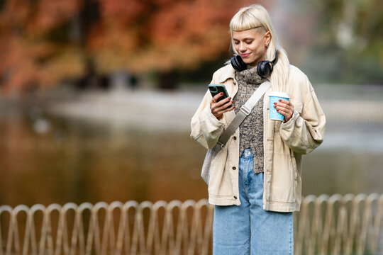Young woman enjoying coffee texting on phone in autumn - Powered by Adobe