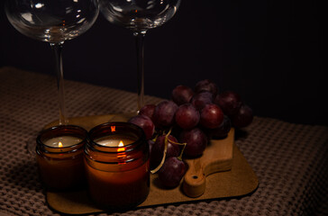 Still life two wine glasses with grapes bunch near romantic aroma burning flame fire candles on a table on dark backround. Decor concept of Christmas holiday celebration with fresh sweet ripe dessert 