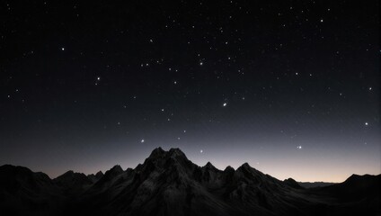 Silhouette of rocky mountain range under a dark, starry night sky with a hint of dawn