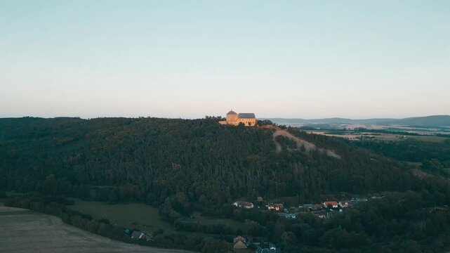 Tocnik Castle stands majestically atop a hill during dusk, surrounded by lush forests and picturesque landscapes. The evening light casts a warm glow over this medieval ruin.