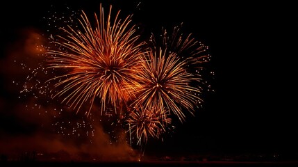 Spectacular orange fireworks explode across the dark night sky, creating a vibrant, celebratory display over a distant, silhouetted landscape