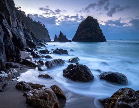 A coastal landscape featuring a rocky beach with waves crashing. Cliffs and sea stacks rise from the water under a dramatic, cloudy sky