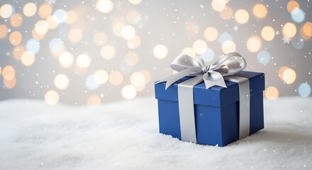 Blue Christmas gift box with silver ribbon standing in snow under falling snowflakes. Winter holiday background symbolizing celebration, surprise, and festive season joy in cold frosty weather.