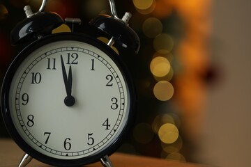 Alarm clock on table against blurred lights, closeup with space for text. New Year greeting card