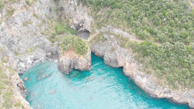 Aerial view of Arcomagno coast in Calabria Italy showing turquoise sea meeting rugged cliffs and hidden caves surrounded by lush Mediterranean vegetation symbolizing untouched natural beauty