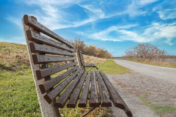 View of two empty wooden park benches on a path beside water, tress and clouds background, sunny, nobody