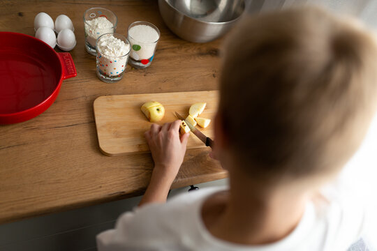 Child preparing apples on wooden board in kitchen