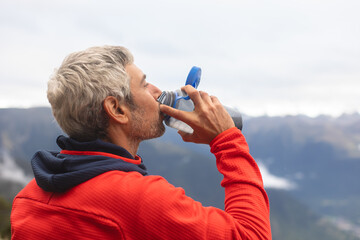 Man in red jacket taking a drink from water bottle outdoors