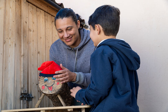 Mother and child decorating a log with a red hat during Tio de Nadal
