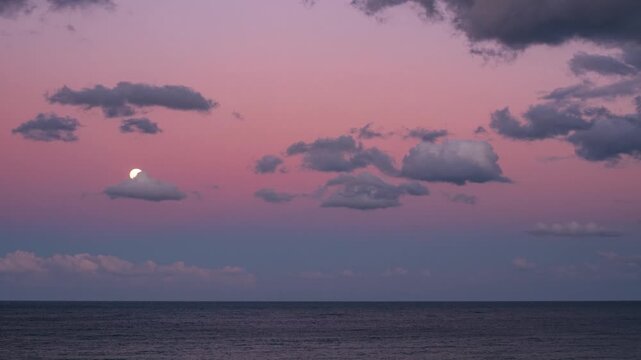 Time lapse: Full moon rising above calm sea under violet pink twilight sky with scattered clouds creating serene atmosphere of peace balance and wonder symbolizing harmony between nature and cosmos