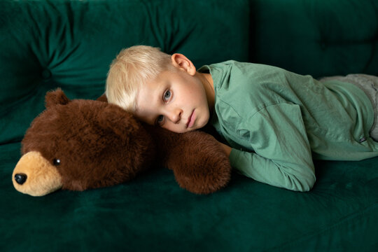Child relaxing with teddy bear on green sofa