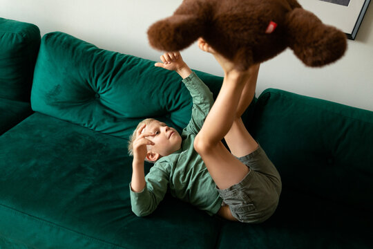 Boy playing with teddy bear on green sofa