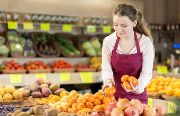 Young woman seller holds ripe tangerines in hands and puts them in a basket on the counter of the vegetable department in the supermarket. Fruit shop worker putting fruit for sale