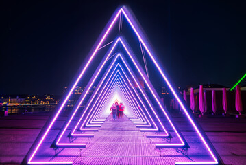 Purple coloured gate of light or purple light tunnel installation made of triangular neon lights at...