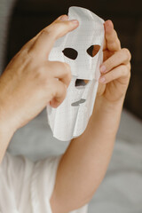 Caucasian female applying skincare sheet mask on face for rejuvenation