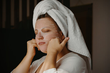 Young caucasian female applying face mask with towel turban at home spa