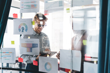 Two colleagues review printed charts on office glass wall, smiling as they discuss tech-enabled...