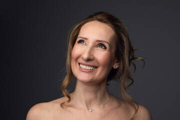 Obraz premium Closeup photo of a happy beautiful woman, looking at camera, holding a hands near neck, isolated grey background.