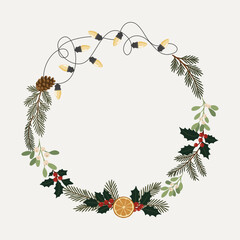 Świąteczna ramka wianek z gałązkami jodły, sosny, ostrokrzewem, jemiołą, plastrem pomarańczy, szyszką i lampkami choinkowymi.