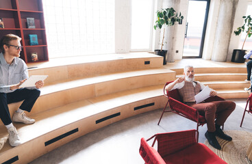 Two businessmen chat by a concrete wall map in modern office. Casual body language and props suggest tech-savvy collaboration and informal knowledge exchange in coworking space.