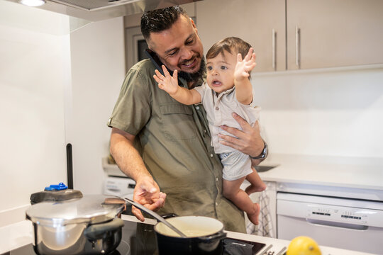 Father multitasking in kitchen while holding son