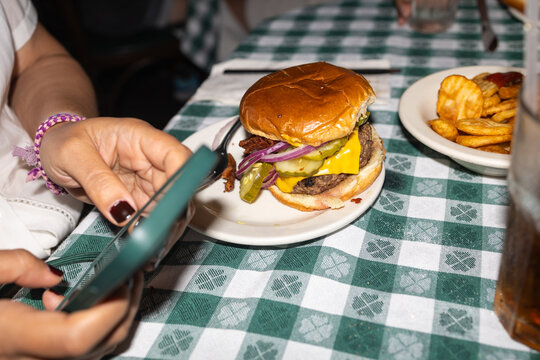 Woman photographing burger with smartphone at a diner table - Powered by Adobe