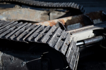 Industrial excavator metal crawler links showing dry mud and dust on surface, compact roller mechanism, traction design and wear marks from continuous construction machinery operation in rugged site