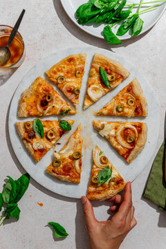 Hand reaching for sliced pizza with cheese and olives