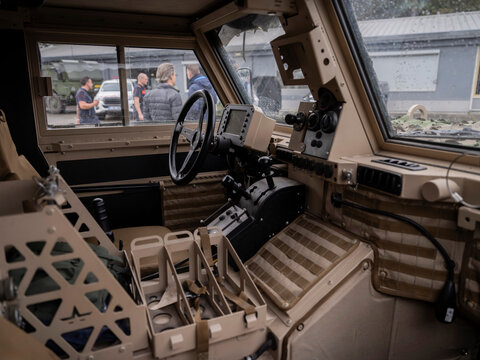 Interior view of military vehicle cockpit showing steering wheel control panel and tactical equipment mounting