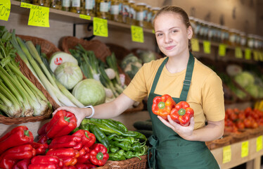 Girl employees in uniform holding fresh bell pepper in grocery shop