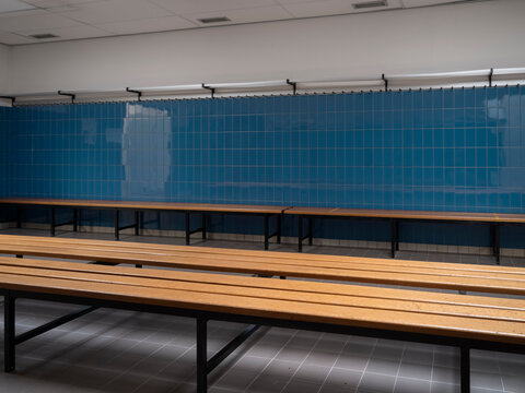 Modern sports facility locker room with blue tile walls wooden benches and organized seating arrangement